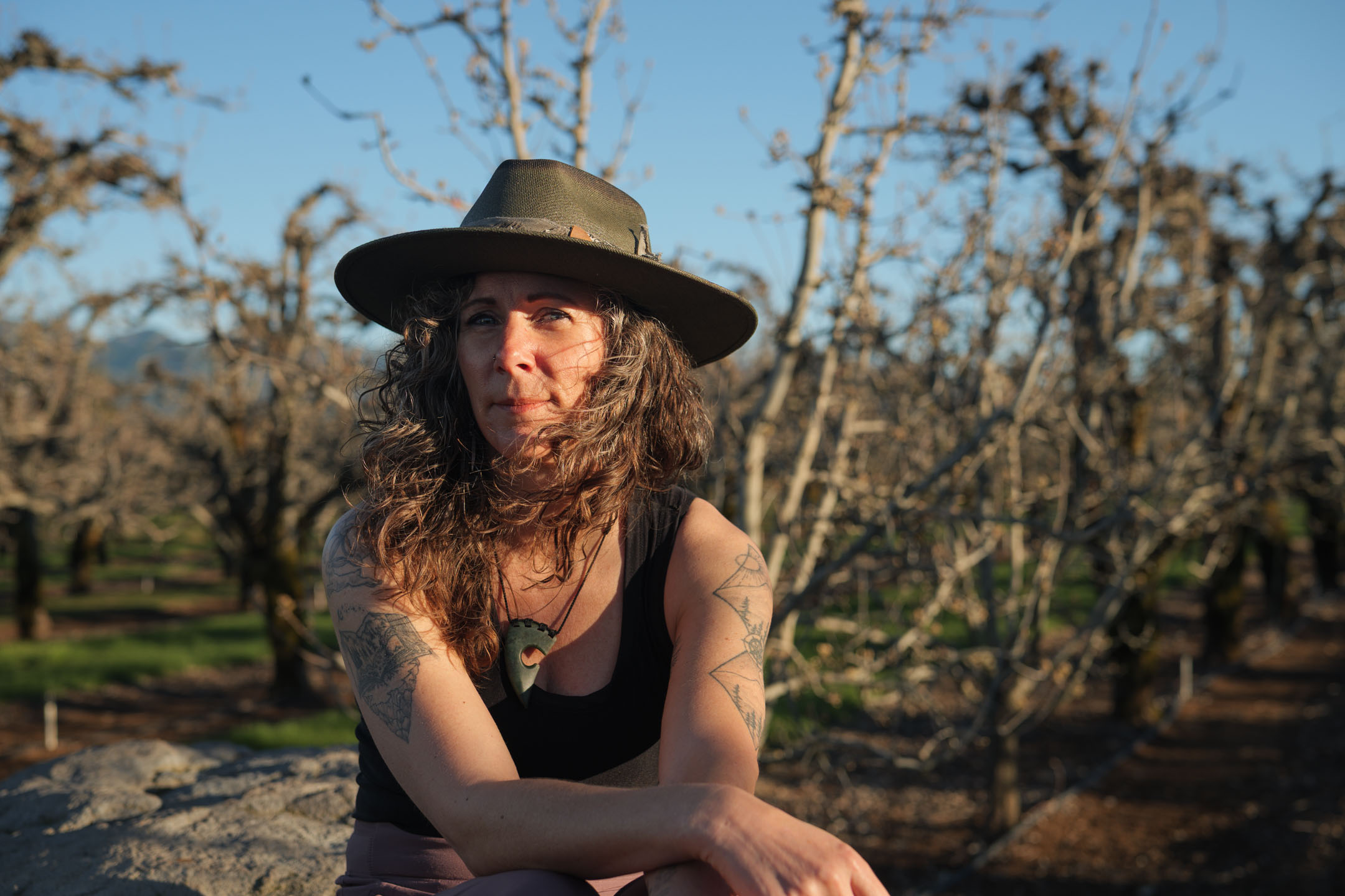 Kate Ensor seated in an orchard wearing a wide-brim hat, looking contemplative
