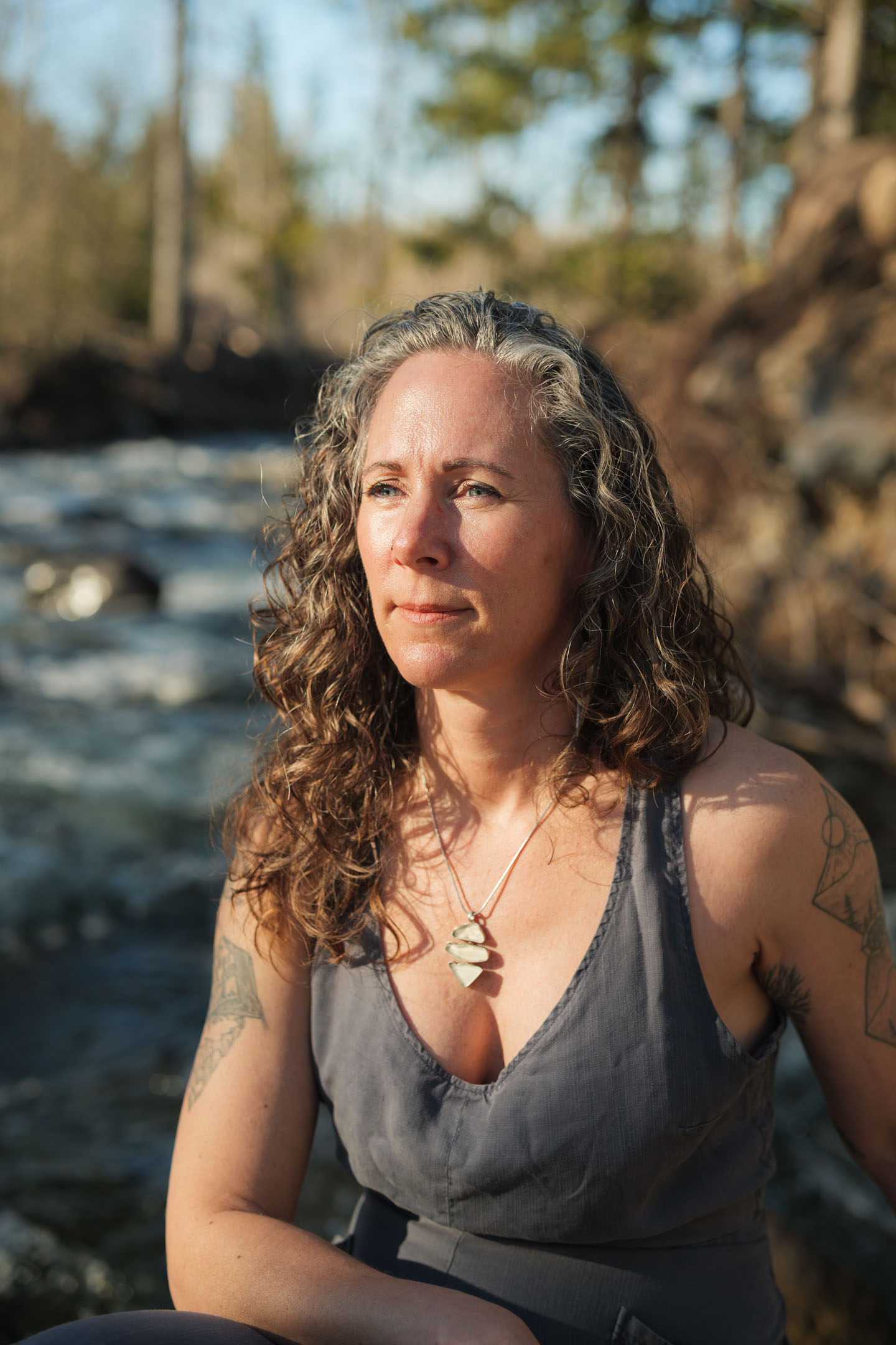 Kate Ensor looking into the distance beside a rushing river, golden light