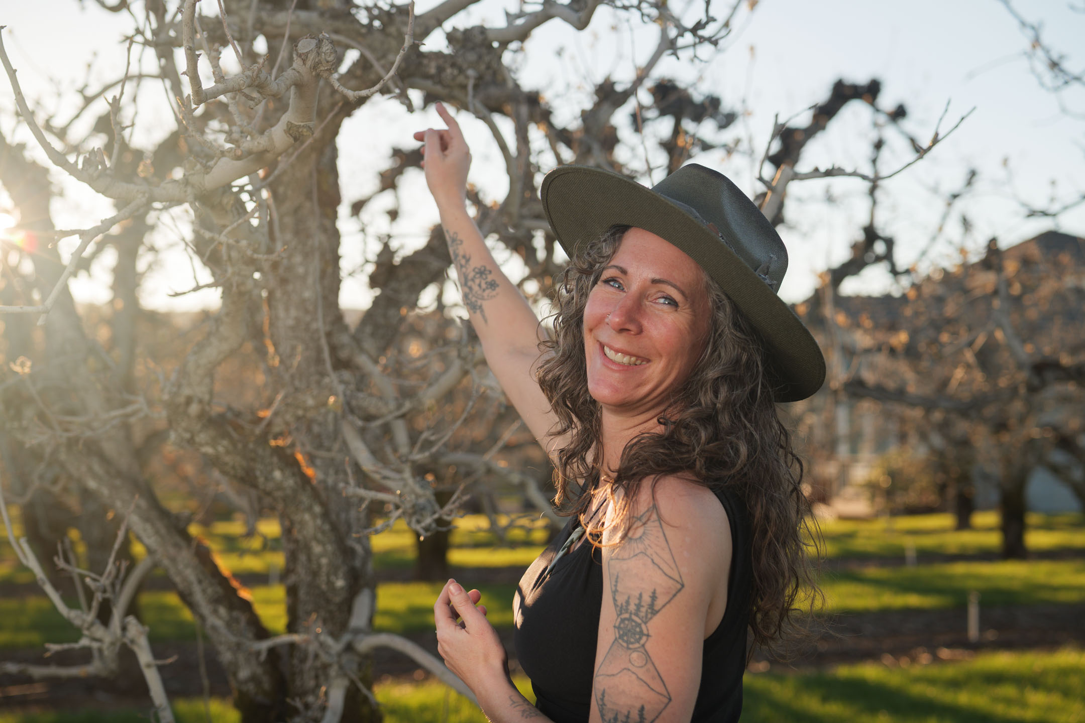 Kate Ensor smiling and reaching upward in the orchard at golden hour